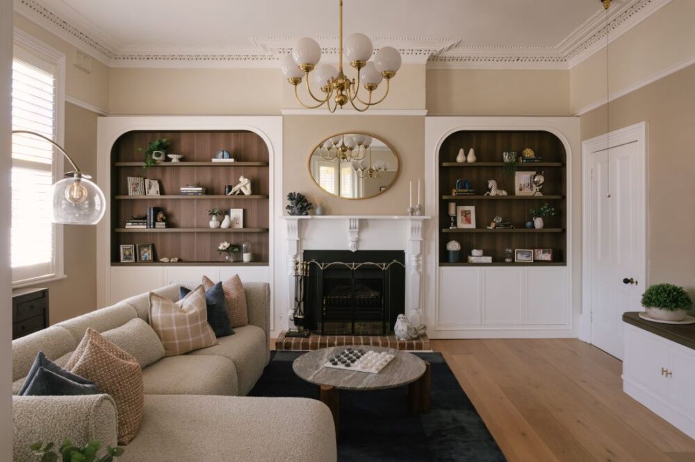 A wide, symmetrical view of the formal living room at Drummoyne House - Issy & H Creative. Features a central black and white heritage fireplace flanked by matching arched recessed bookshelves with dark wood timber backing, balanced by a modern curved bouclé sectional sofa and glass dome floor lamp.