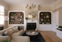 A wide, symmetrical view of the formal living room at Drummoyne House - Issy & H Creative. Features a central black and white heritage fireplace flanked by matching arched recessed bookshelves with dark wood timber backing, balanced by a modern curved bouclé sectional sofa and glass dome floor lamp.