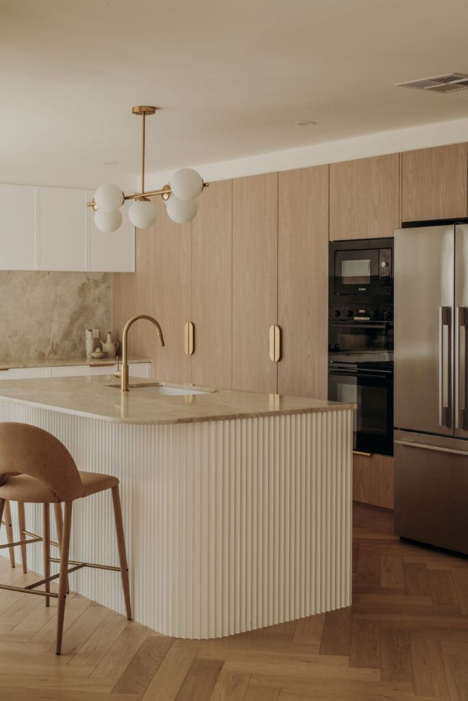 Elegant kitchen island with ribbed details and modern lighting by Sabina Christine Interiors at 48 Bilwara Avenue.