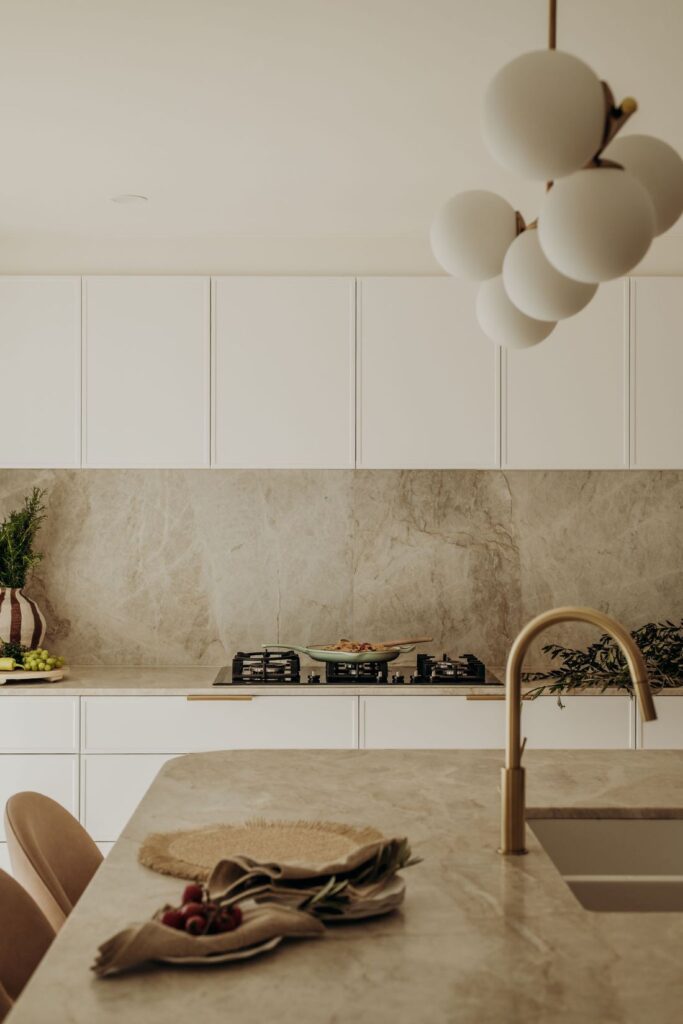Contemporary kitchen with marble backsplash, golden faucet, and chic lighting by Sabina Christine Interiors at 48 Bilwara Avenue.