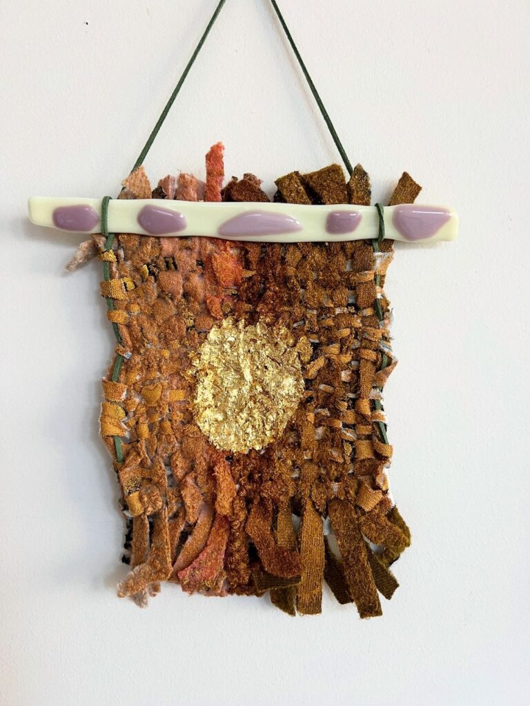 Handwoven textile wall hanging in warm earthy tones with gold centre