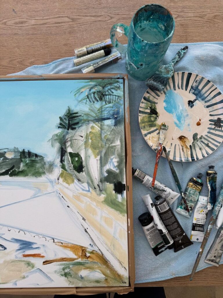 Top-down view of abstract landscape painting with brushes, paint tubes, and palette on studio table