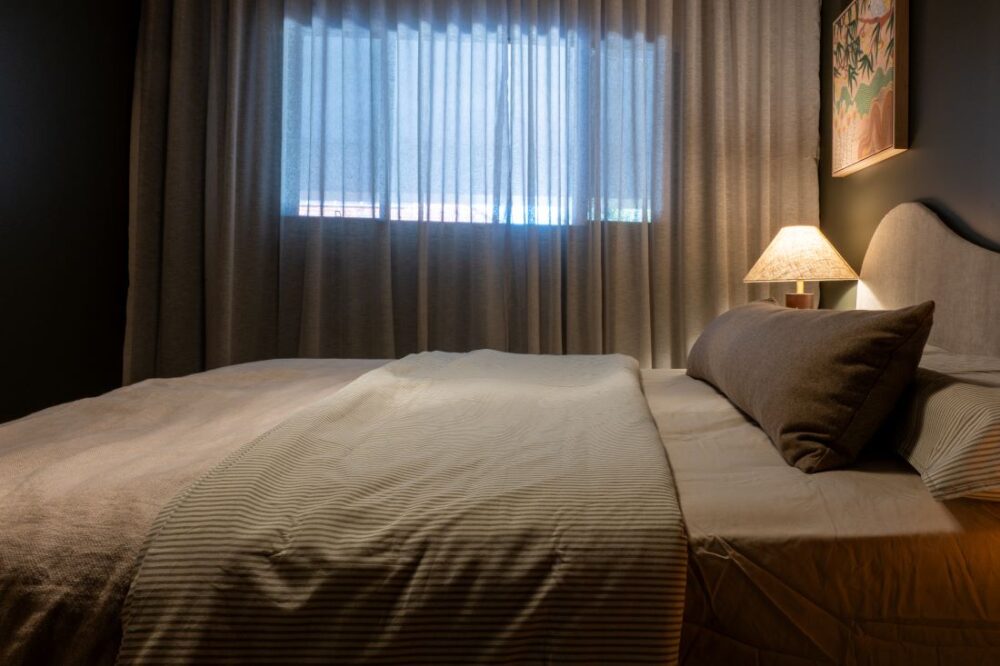 Bed with neutral linens and sheer curtains in dark green bedroom