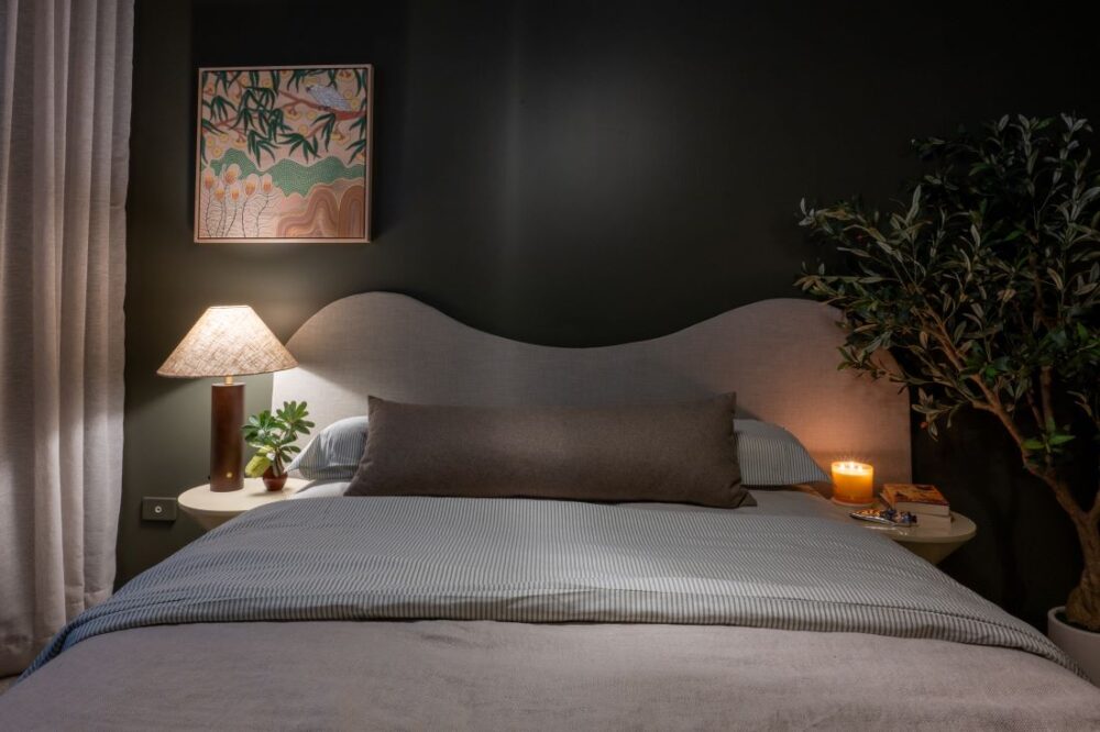 Bed with curved headboard, dark green walls, and bedside lighting