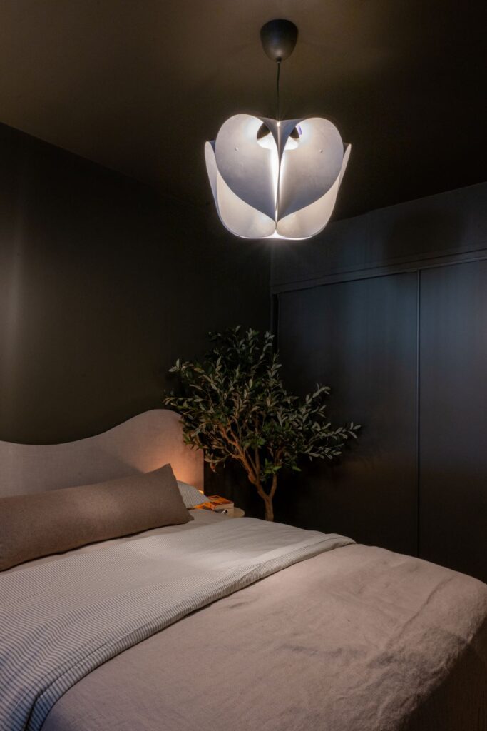 Bedroom with dark green walls, curved bed, and sculptural pendant light