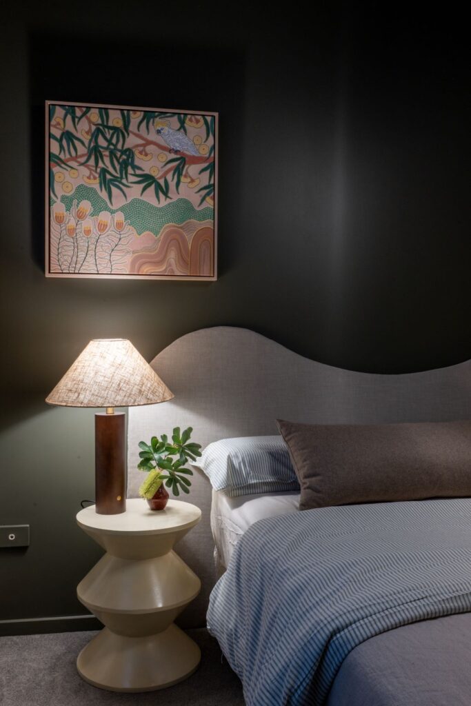 Bed with neutral linens, side table, lamp, and framed artwork
