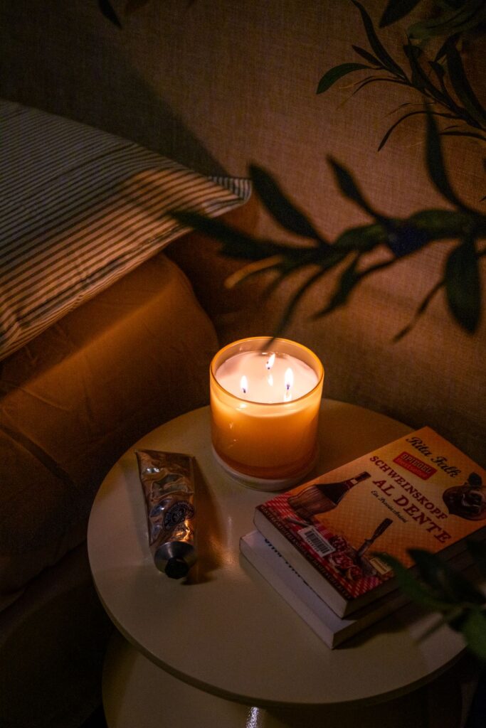 Bedside table with lit candle, books, and soft pillow