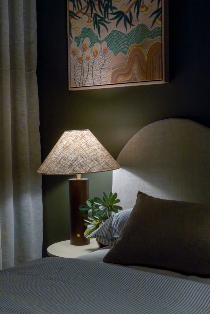 Bedside table with lamp, potted plant, and framed artwork above bed