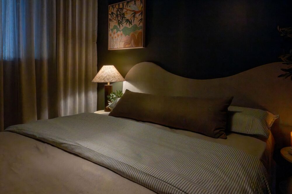 Bed with neutral linens, dark green wall, and soft bedside lighting