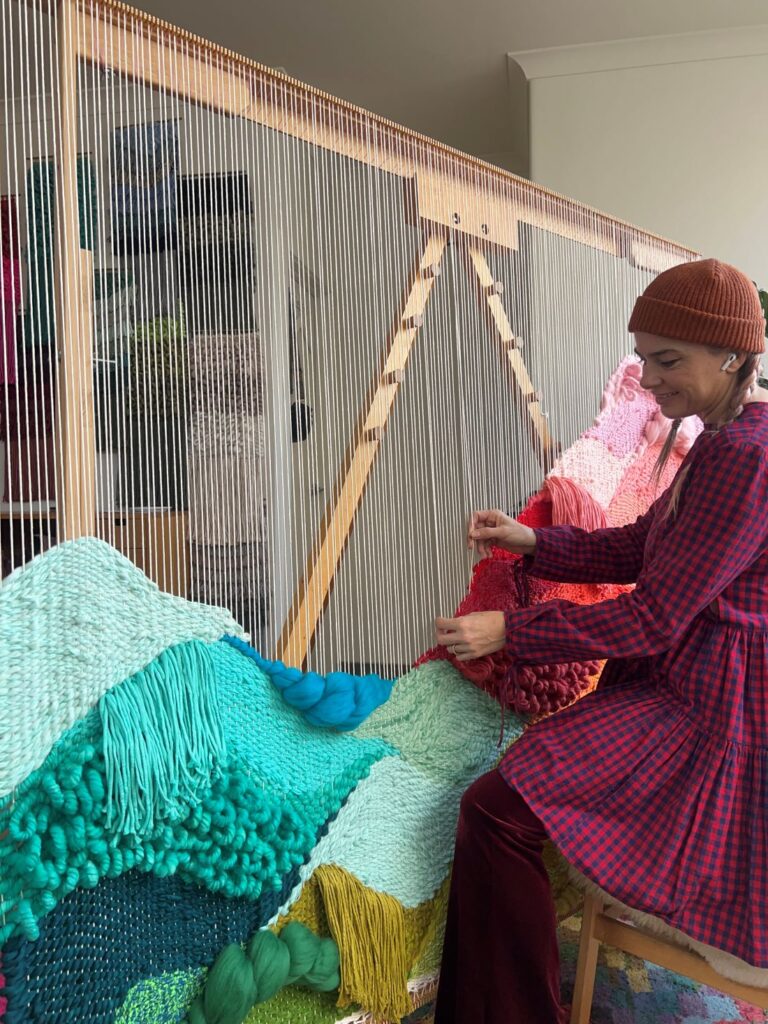 Artist weaving a colorful textile on a large loom
