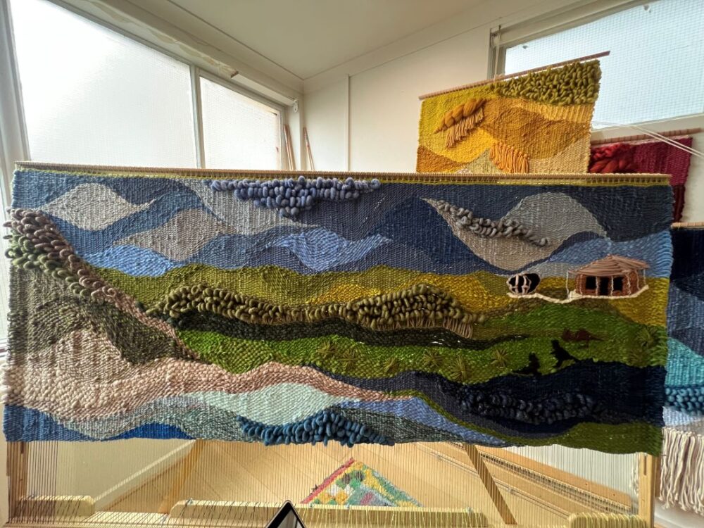 Large handwoven textile depicting layered landscape in blue and green tones