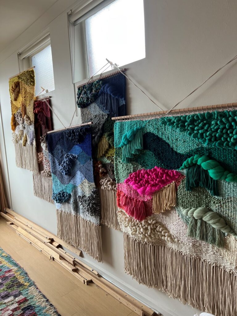 Row of colorful handwoven textile artworks displayed on a studio wall