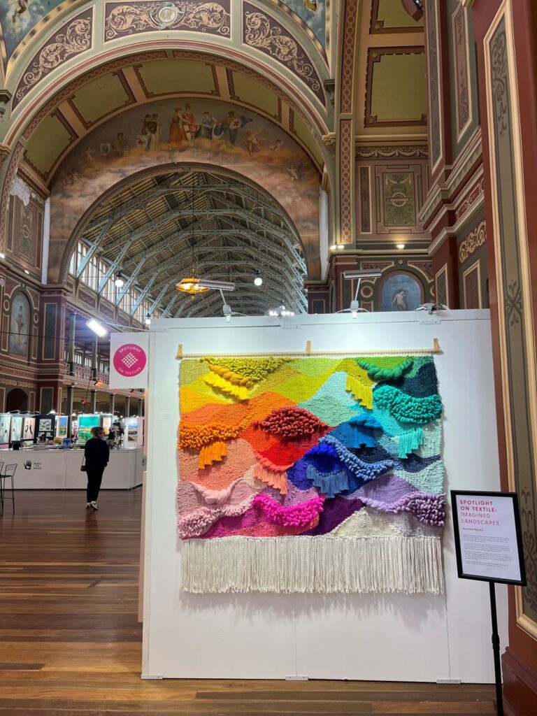 Large colourful woven textile artwork displayed in historic gallery space