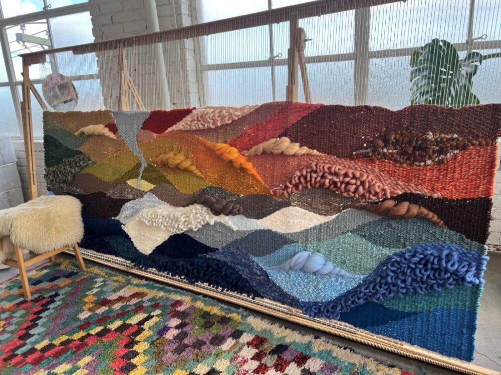 Large handwoven textile artwork with layered landscape textures in warm and cool tones