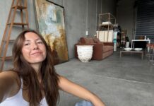 Painting calm: The atmospheric abstract art of Jennifer Lia Taking a selfie in a minimalist studio surrounded by abstract paintings and furniture