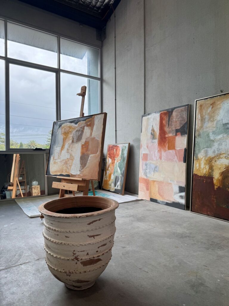 Abstract paintings leaning against studio wall with ceramic planter in foreground