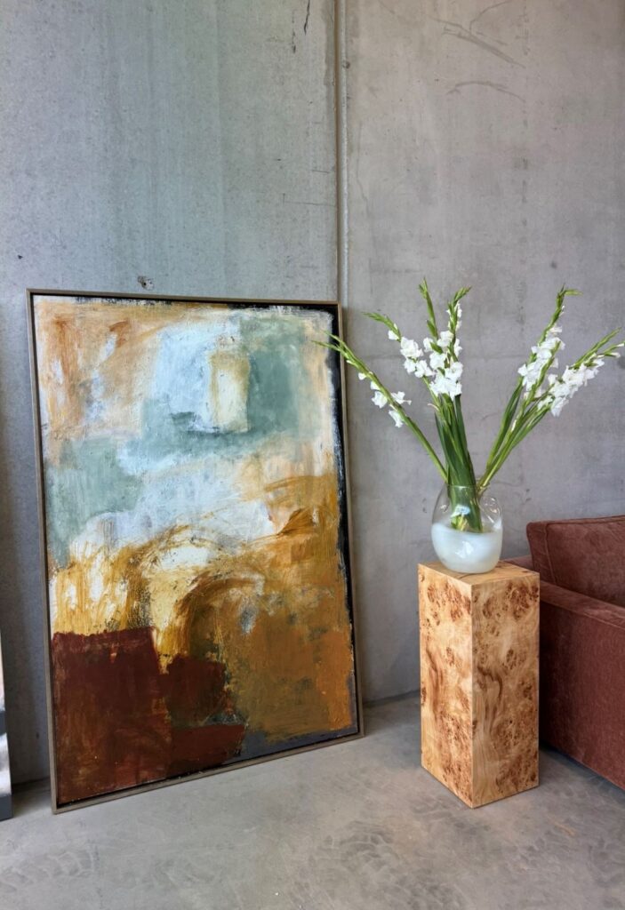 Large abstract painting leaning against a concrete wall beside a vase of white flowers on a pedestal