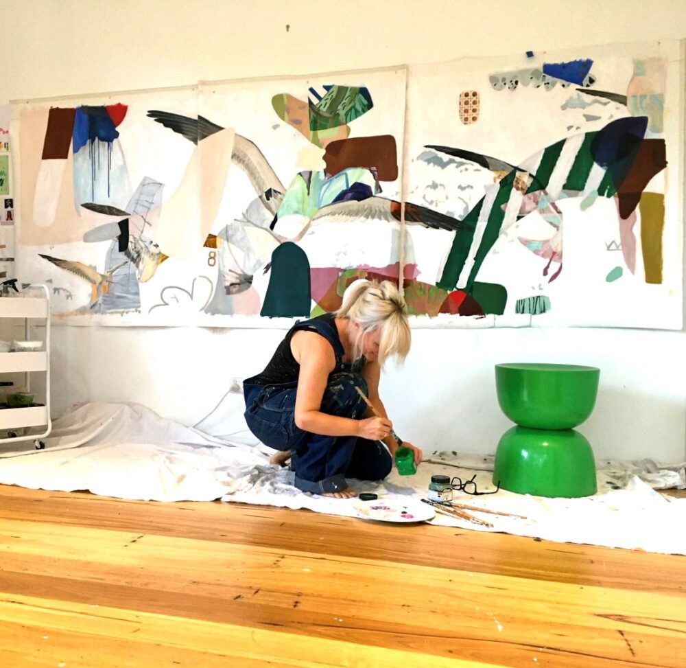Artist painting abstract collage-style mural on wall in studio