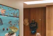 Artist sitting on bench beside large blue abstract figurative painting in hallway