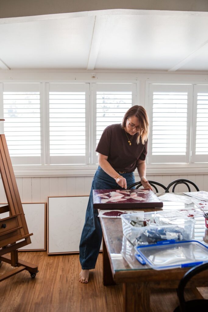 Self-taught artist applying paint with a palette knife to a textured bird artwork in her dining room studio
