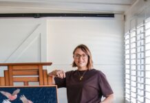 The textural pared back palette knife art of Tanya Boyes Artist Tanya Boyes standing beside a textured painting of pink galahs displayed on an easel in her Dalby home studio