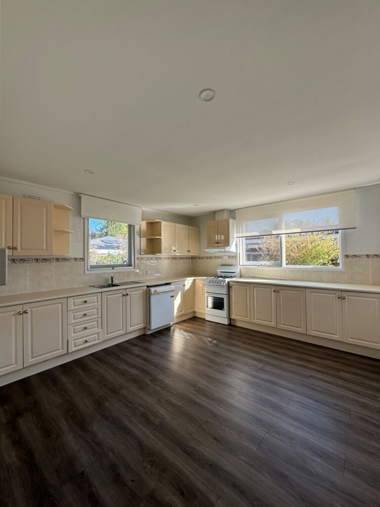 Bright open kitchen interior with cream cabinetry, dark timber flooring, tiled splashback, large windows and natural light.