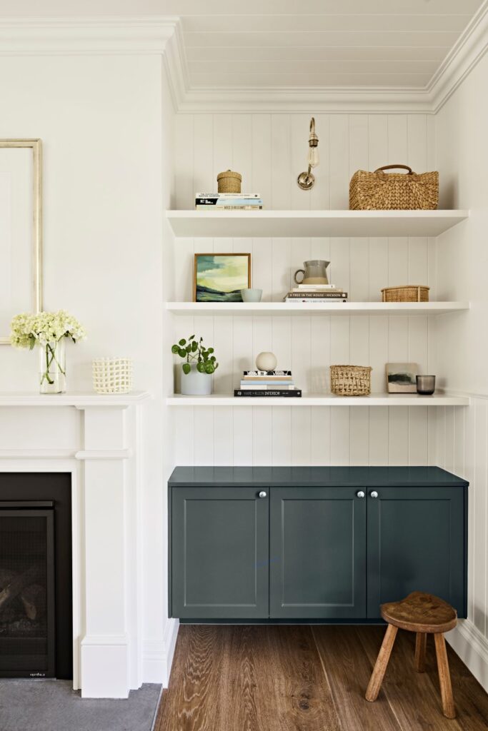 White open shelving styled with books, baskets and ceramics above dark blue built-in cabinetry beside a fireplace
