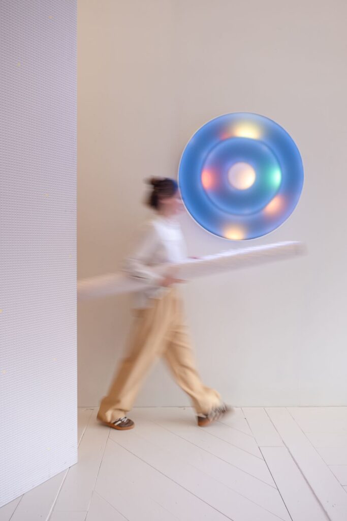 Blurred woman walking past a blue circular wall light glowing with soft multicoloured points