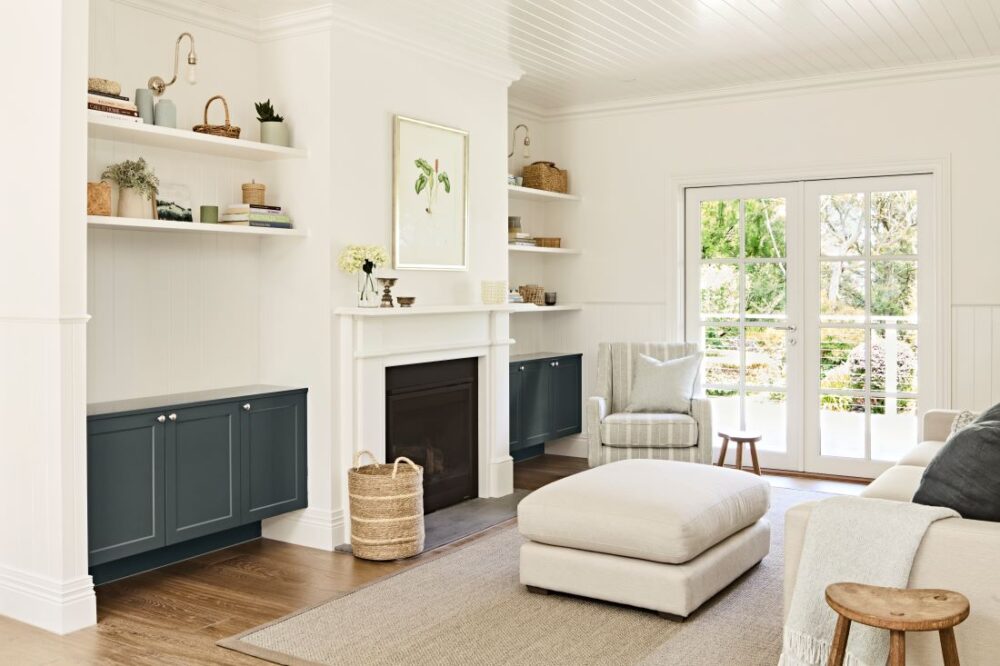 Light-filled sitting room with a white fireplace, dark blue built-in cabinetry, open shelving and French doors overlooking the garden