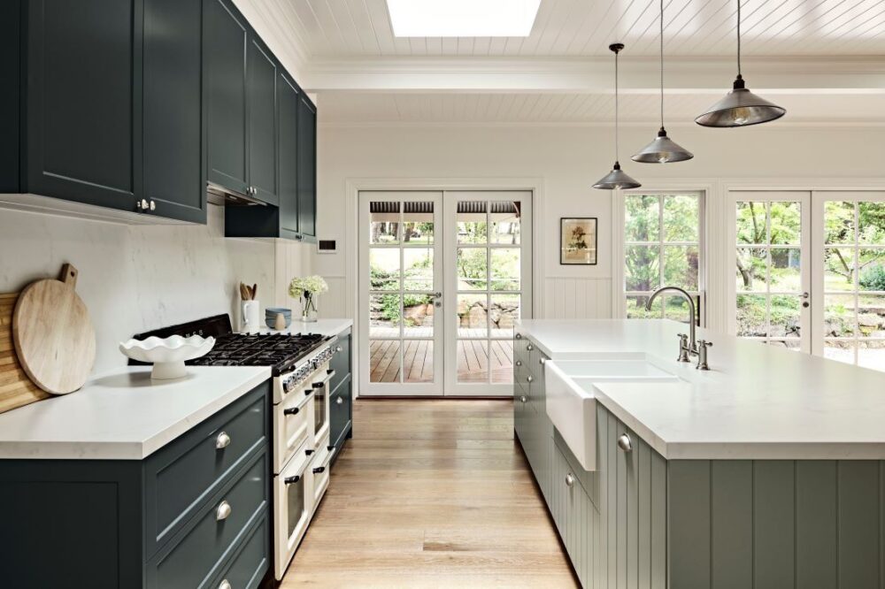Light-filled country kitchen with dark navy cabinetry, a sage green island, white stone benchtops and French doors opening to the garden