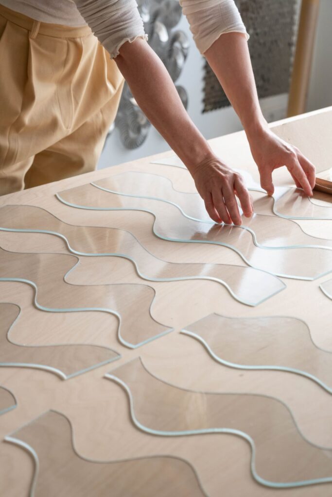 Arranging clear wavy glass pieces across a timber worktable in the studio