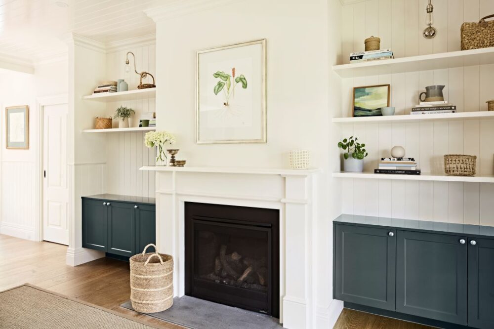 White fireplace flanked by dark blue built-in cabinetry and open shelves styled with books, baskets and decorative objects