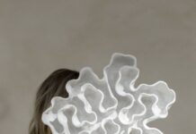 Shaped by the sea: The ceramic art of Michelle Morton Michelle Morton holding a large white ceramic sculpture with layered, undulating forms in front of her face.