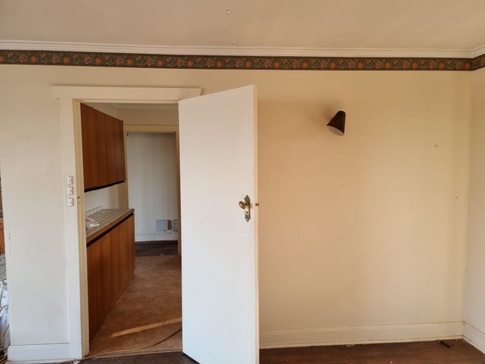 Empty living room looking into old kitchen