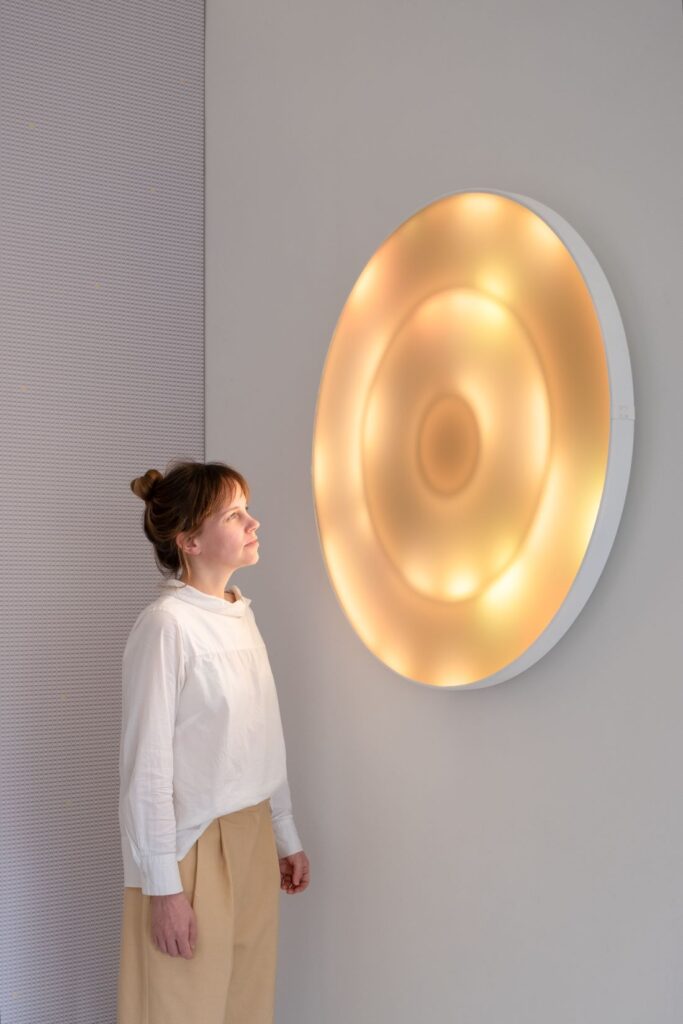 A+N Studio designer viewing a circular wall-mounted light installation glowing in warm amber