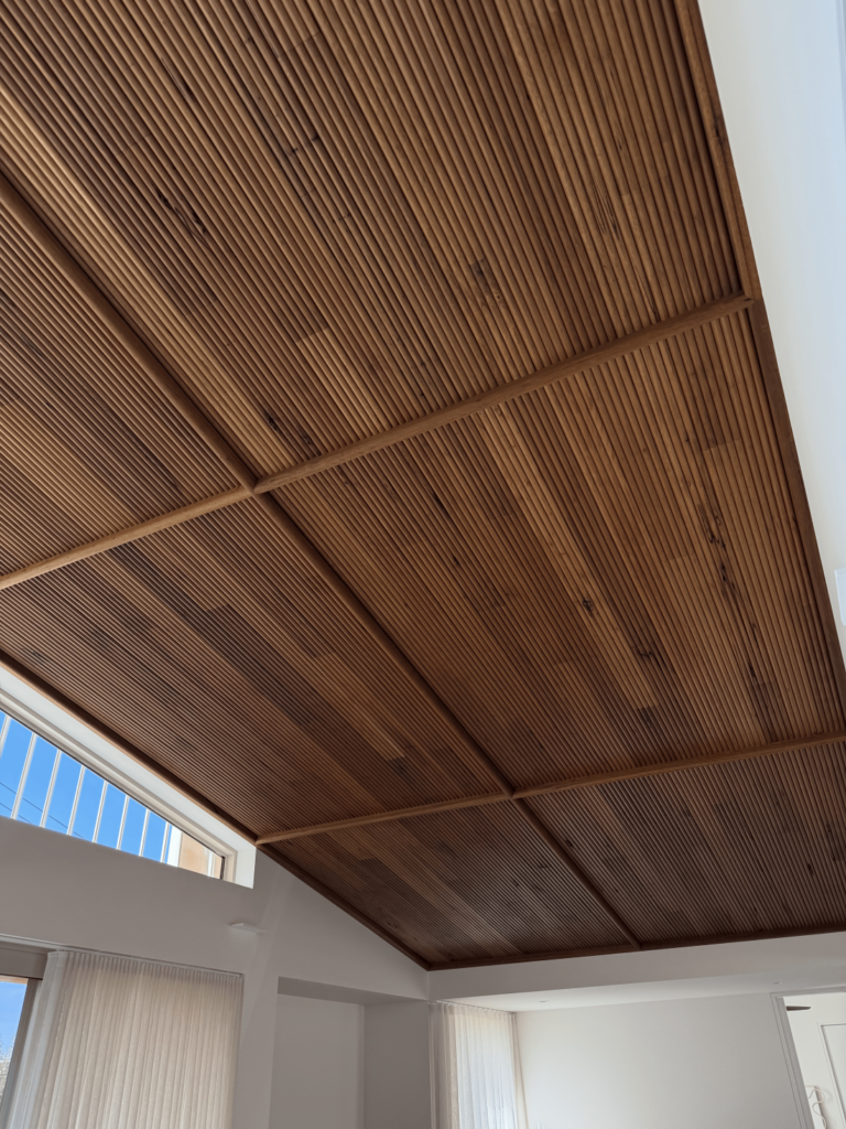 Slatted timber batten ceiling detail in a light-filled contemporary home with white walls, sheer curtains and clerestory windows.