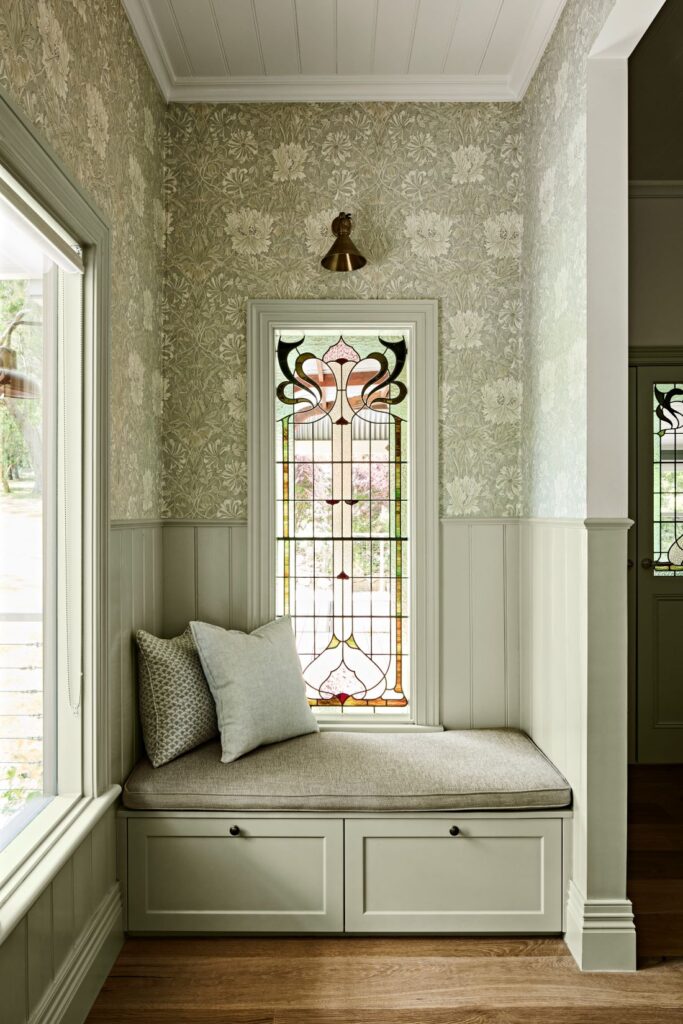 Built-in window seat beneath a decorative stained glass window with sage wall panelling and floral wallpaper