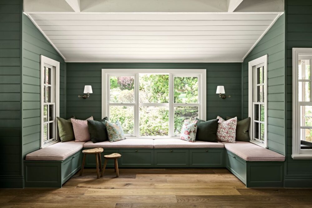 U-shaped built-in window seat with patterned cushions, deep green panelled walls and garden