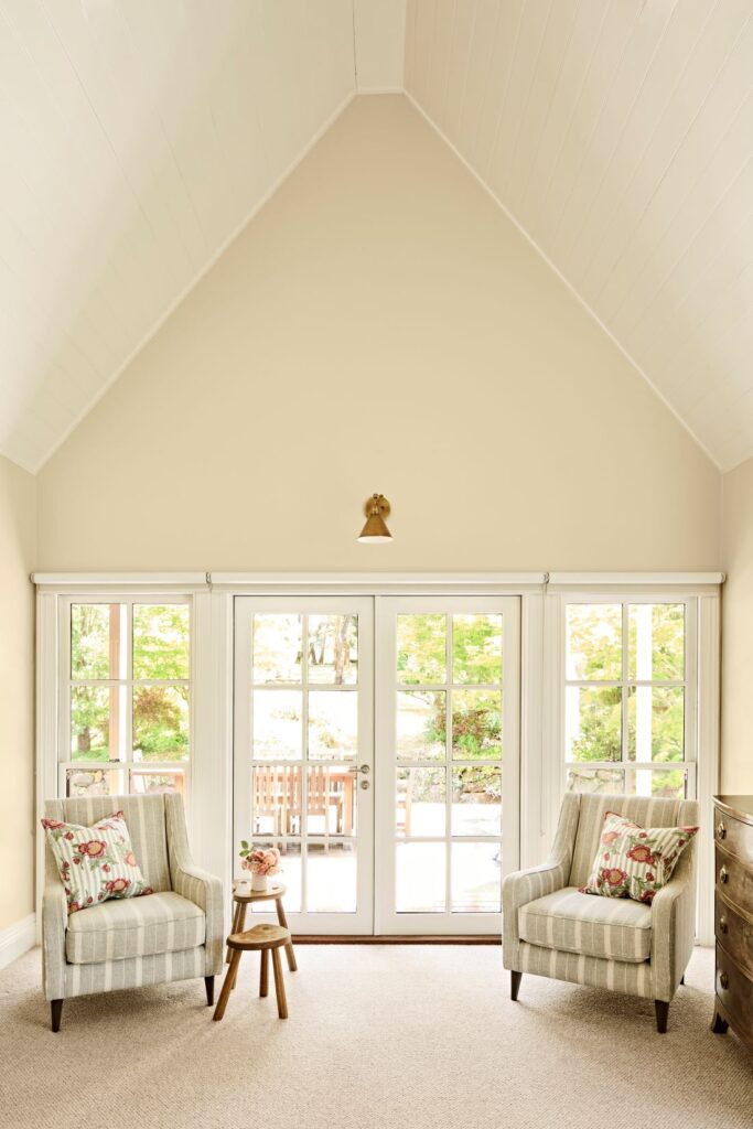 Light-filled sitting area with two striped armchairs, floral cushions and French doors beneath a vaulted white lining-board ceiling