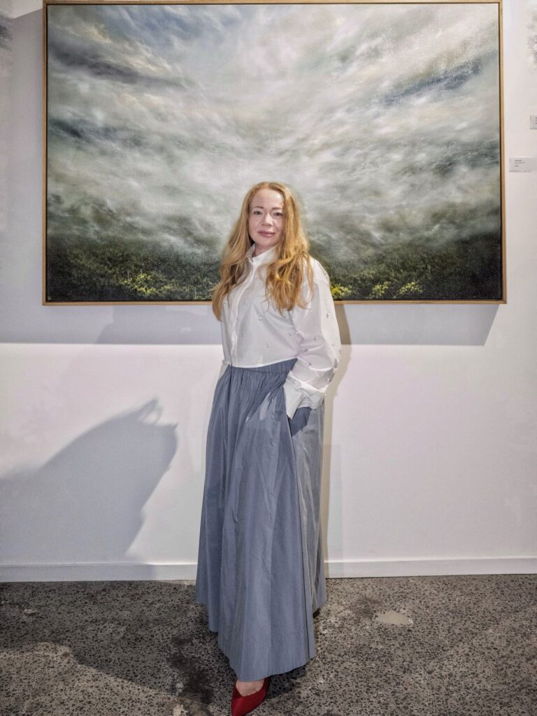 Artist Kelly Kondis standing in front of large oil landscape
