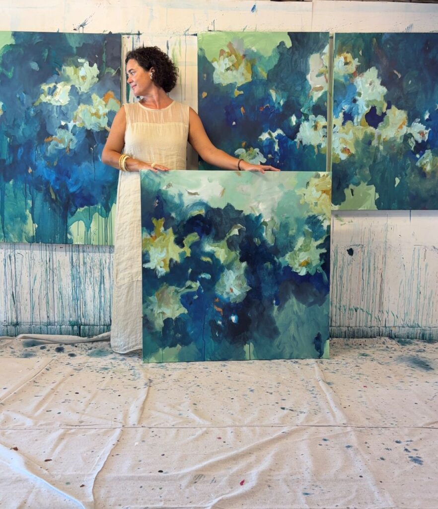 Artist holding square abstract canvas in paint-splattered studio