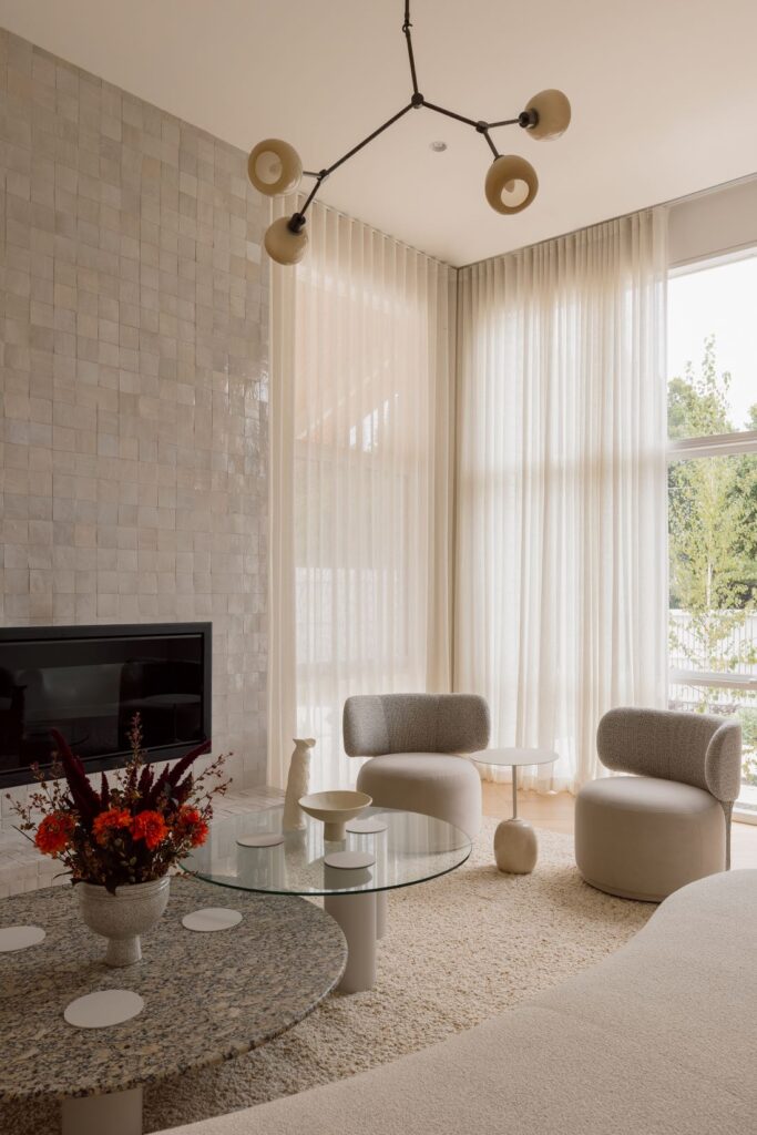 Formal living room in Hampton with a textured Zellige tiled fireplace, curved cream armchairs, sculptural pendant light and sheer curtains
