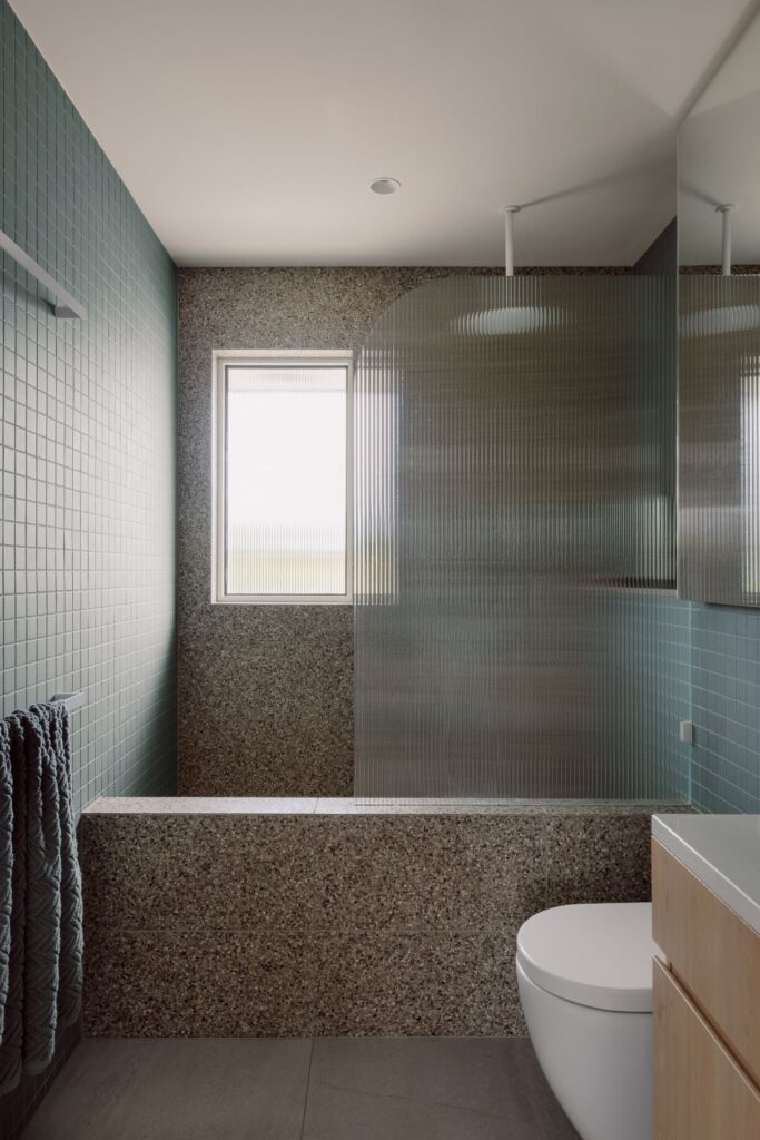 Hampton bathroom with green wall tiles, terrazzo bath surround, fluted glass shower screen and white toilet.