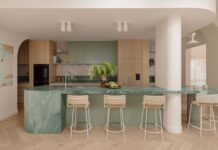 A textural contemporary home that’s refined yet deeply liveable Hampton kitchen with a curved green quartzite island, pale timber cabinetry, arched ceiling details and herringbone timber flooring.