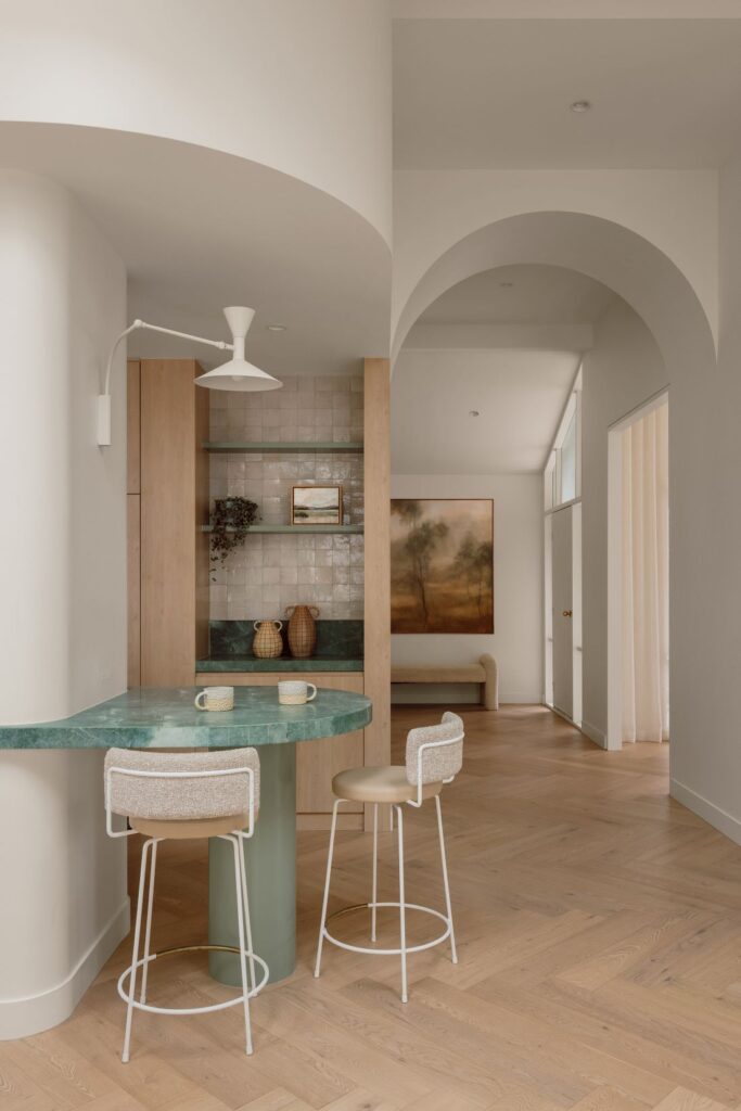 Hampton kitchen with a curved green quartzite island, pale timber cabinetry, Moroccan zellige tiles and arched openings.