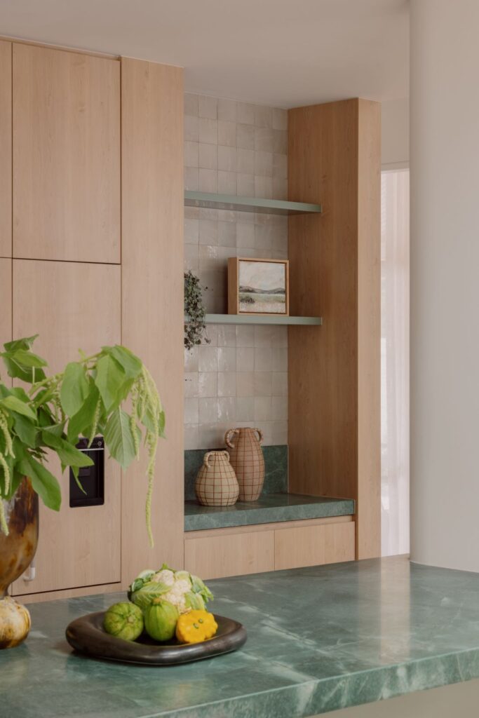 Hampton kitchen with green quartzite benchtops, pale timber cabinetry, Moroccan zellige tiles and open display shelving.