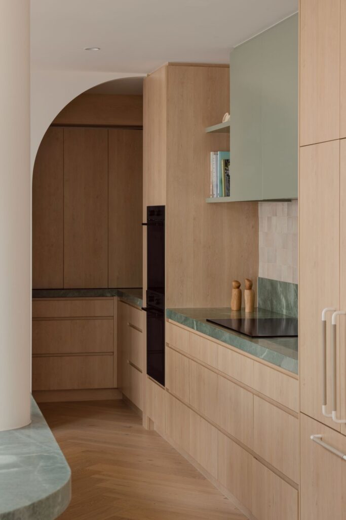 Hampton kitchen with pale timber cabinetry, green quartzite benchtops, soft green overhead cupboards and arched timber joinery.