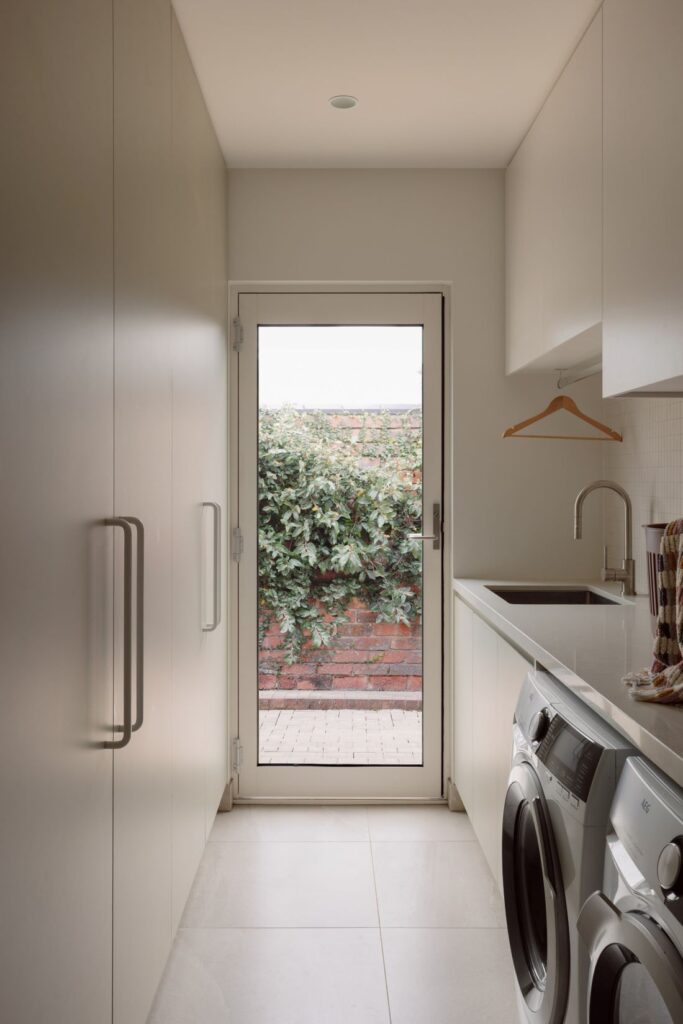 Hampton home laundry with white built-in cabinetry, integrated washing machines, utility sink and garden access.