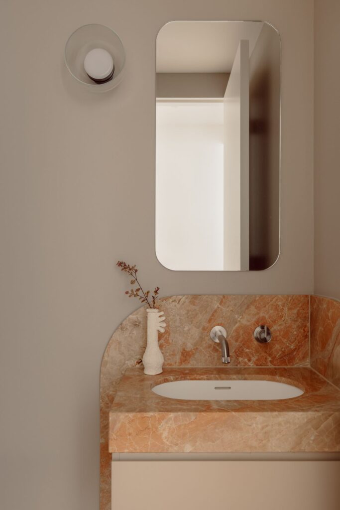 Hampton powder room with a peach-toned marble vanity, curved splashback, rounded mirror and wall-mounted tapware.