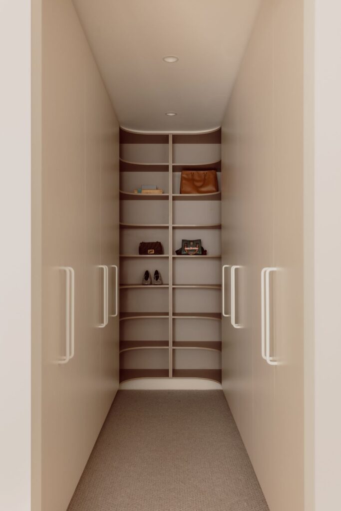 Hampton home walk-in wardrobe with curved shelving, built-in cabinetry, warm neutral finishes and integrated storage.